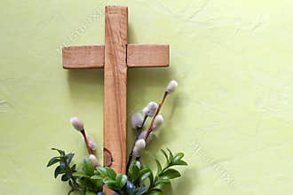 Wooden cross with boxwood twigs and catkins on green background. Palm Sunday concept