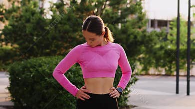 A young sportive woman does morning exercises, stretches legs and neck before workout in the city park area. An athlete