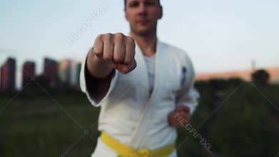 Karate athlete practicing kicks wearing kimono outdoor at sunset. Sporty man training martial arts.