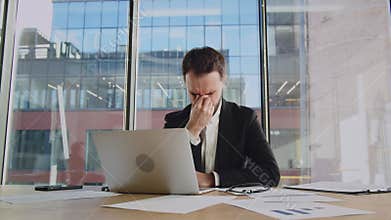 Concentrated businessman trader are tired. The man takes off his glasses and rubs his tired eyes. Sits at laptop