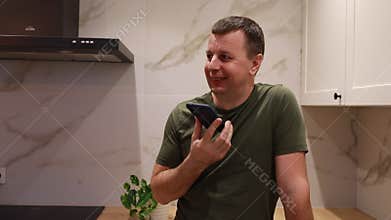 Man in Kitchen Demonstrates Voice Assistant Interaction on Smartphone