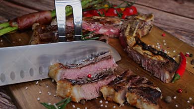 T- bone steak grill cut into pieces with knife on cutting board. Close up. Slow motion