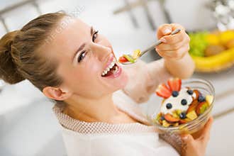 Happy young housewife eating fruits salad