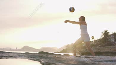 Beautiful woman playing volleyball with herself at sunset by the sea