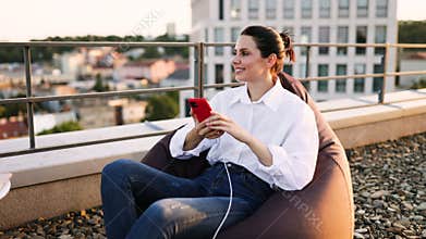 Businesswoman sitting on beanbag chair while charging phone outdoors