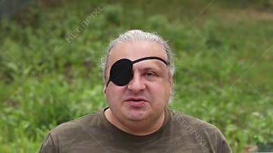 A blind, visually impaired man with a black medical patch on his eye looks at his phone and scrolls through his