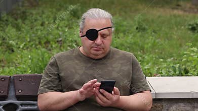A blind, visually impaired man with a black medical patch on his eye looks at his phone and scrolls through his
