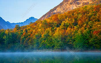 the beautiful autumn forest with its thousand colors is reflected in the lake with a light morning mist
