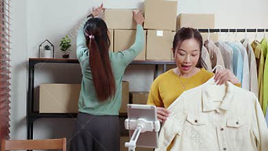 Two young asian woman live online clothing store while showing clothing with tablet on social at home.