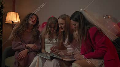 Group of young women friends and bride celebrating bachelorette party at home, bride and bridesmaids sit on sofa and