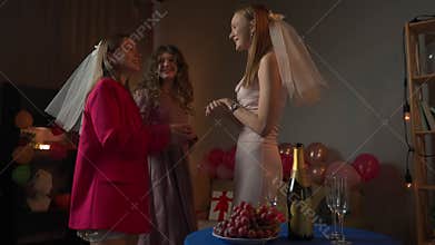 Group of young women friends and bride celebrating bachelorette party at home, bridesmaids dressed in veils waiting for