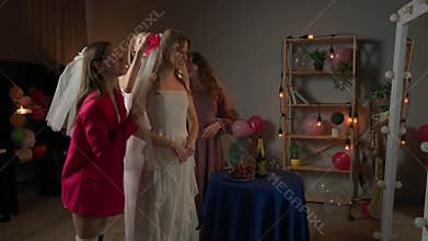Group of young women friends and bride celebrating bachelorette party at home, girls help the bride to put on veil