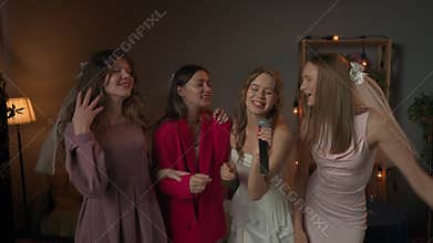 Group of young women friends and bride celebrating bachelorette party at home, bride and bridesmaids having fun, singing