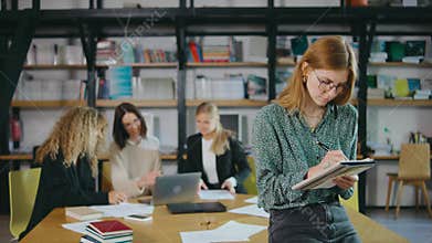 portrait of a young beautiful girl businesswoman writes something in a notebook. A group of girls work in the library