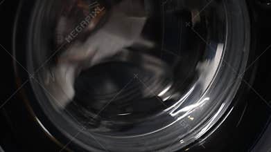 Washing machine drum rotating with socks and laundry detergent inside, offering glimpse into everyday chore of laundry