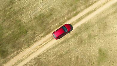 A car drives through the ruts of a dusty dirt road across wild deserts fields.