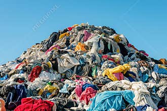 Massive pile of discarded clothing under a clear blue sky reflects fast fashion waste and environmental impact