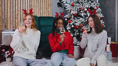Three friends in festive attire celebrate the holidays with cheerful drinks around a beautifully decorated Christmas