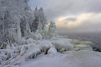 Winter landscape in Karelia: snow-covered forest, icy coastline and dark lake water