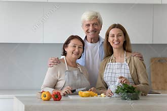Happy mature old parents and adult kid cooking family dinner
