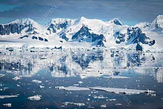 Stunning snowy landscape with mountains reflecting in the water of Hanusse Bay, Antarctica.