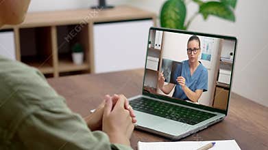 A patient at home in a relaxed setting, engaged in a virtual medical consultation on a laptop with a smiling doctor, who