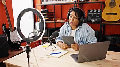 Smiling woman podcasting with microphone, tablet, and laptop in a music studio setup