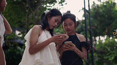 Two young Asian teenage girls next to each other looking at each other's smartphone in the garden in summer