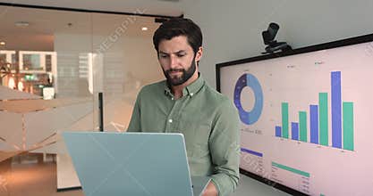 Analyst brainstorming working on laptop standing against charts data screen