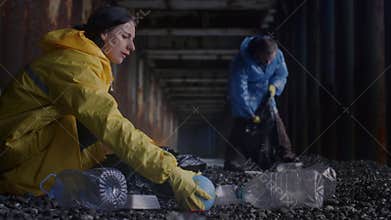 Responsible couple in raincoats engages in collecting litter into garbage bags cleaning shore