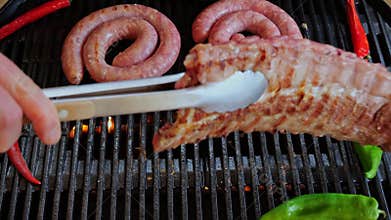 Chef turns over pork ribs On Grill. Cooking natural sausage on grill. Slow motion. Close up