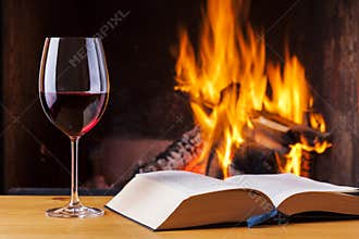 Red wine and book at cozy fireplace