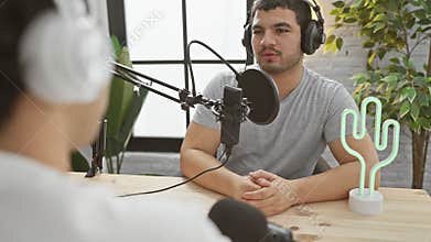 Two men engaged in a conversation at a modern podcasting studio, one speaking into a microphone