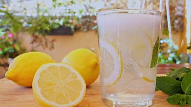 Drink with gas is poured into a glass with ice, lemon and mint. Slow motion. Outdoors