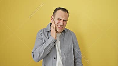 Young hispanic man in shirt touching aching tooth with painful expression, standing isolated on yellow background amidst dental