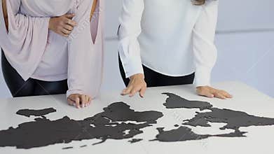 Hands of two women which assemble world map puzzle