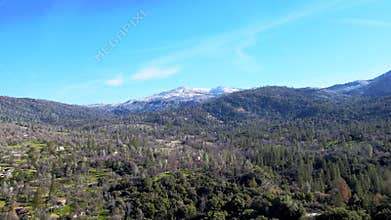 Aerial view of Yosemite National Park, lush green forests, rolling hills, snow-capped mountains, clear blue sky, serene landscape