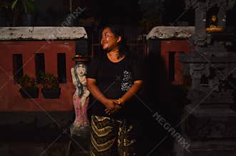 A Balinese woman smiling while standing in front of a traditional temple shrine at night