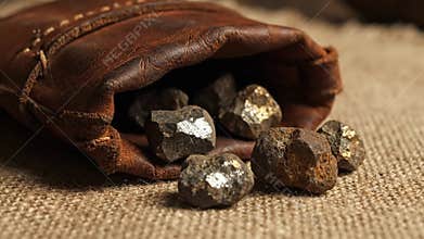 Raw Pyrite Rocks Tumble from Leather Bag on Burlap Background with Warm Studio Lighting Mining Business and Gold Rush