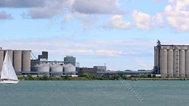 Sailboat sailing past industrial plant on Detroit river at the border of Detroit and Windsor, Canada