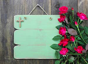 Rustic green blank sign with wooden cross and flower border of red roses hanging on wood door