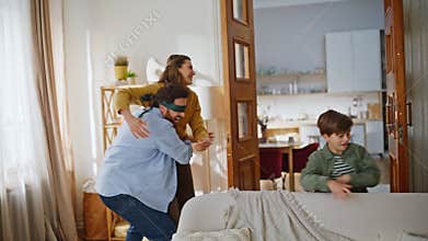 Playful father catching mother wearing blindfold hugging living room closeup