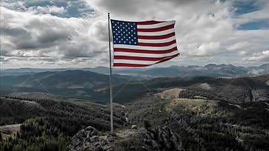 American flag waving majestically on a flagpole atop rugged mountain peak, with expansive forest and cloud filled sky for