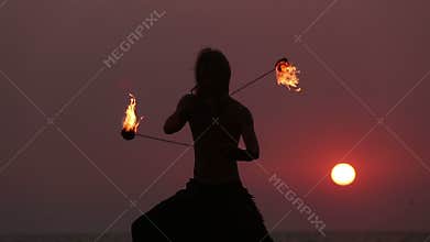 Male Artist of the spins fire poi on a rock