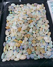 Colorful opal gemstones displayed in a tray at a gem show in a market setting during a sunny afternoon