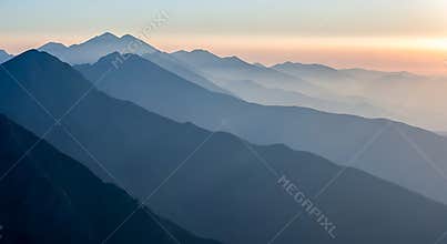 Layered blue mountain ranges fade into soft pastel sky at dawn landscape nature