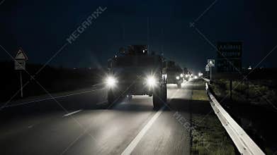 Military armored vehicle convoy driving on a highway at night