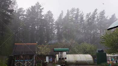 Rain And Fog Engulf Rural Dacha And Forest. Smoke Rises From Chimney On Gloomy Day.