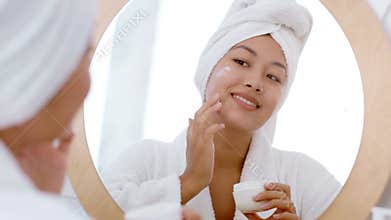 Young woman enjoys skin care routine at home while pampering herself