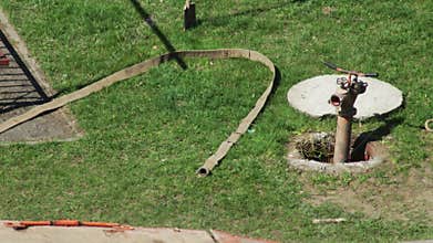 Male worker connects hose to hydrant in sewer well, industry. Copy space for text, grass